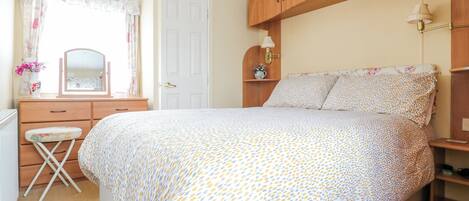 A bedroom with a bed, a dresser, a mirror, a window with curtains, and a nightstand with a lamp.