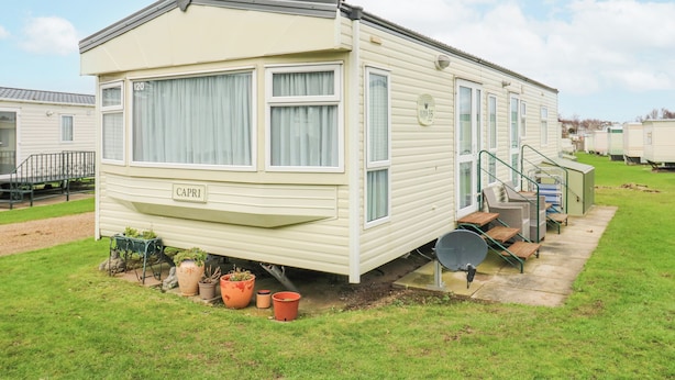 A mobile home with a ramp leading to the entrance, a small patio area with potted plants, and a sign indicating the unit number. - 120 Caravan (Great Yarmouth)