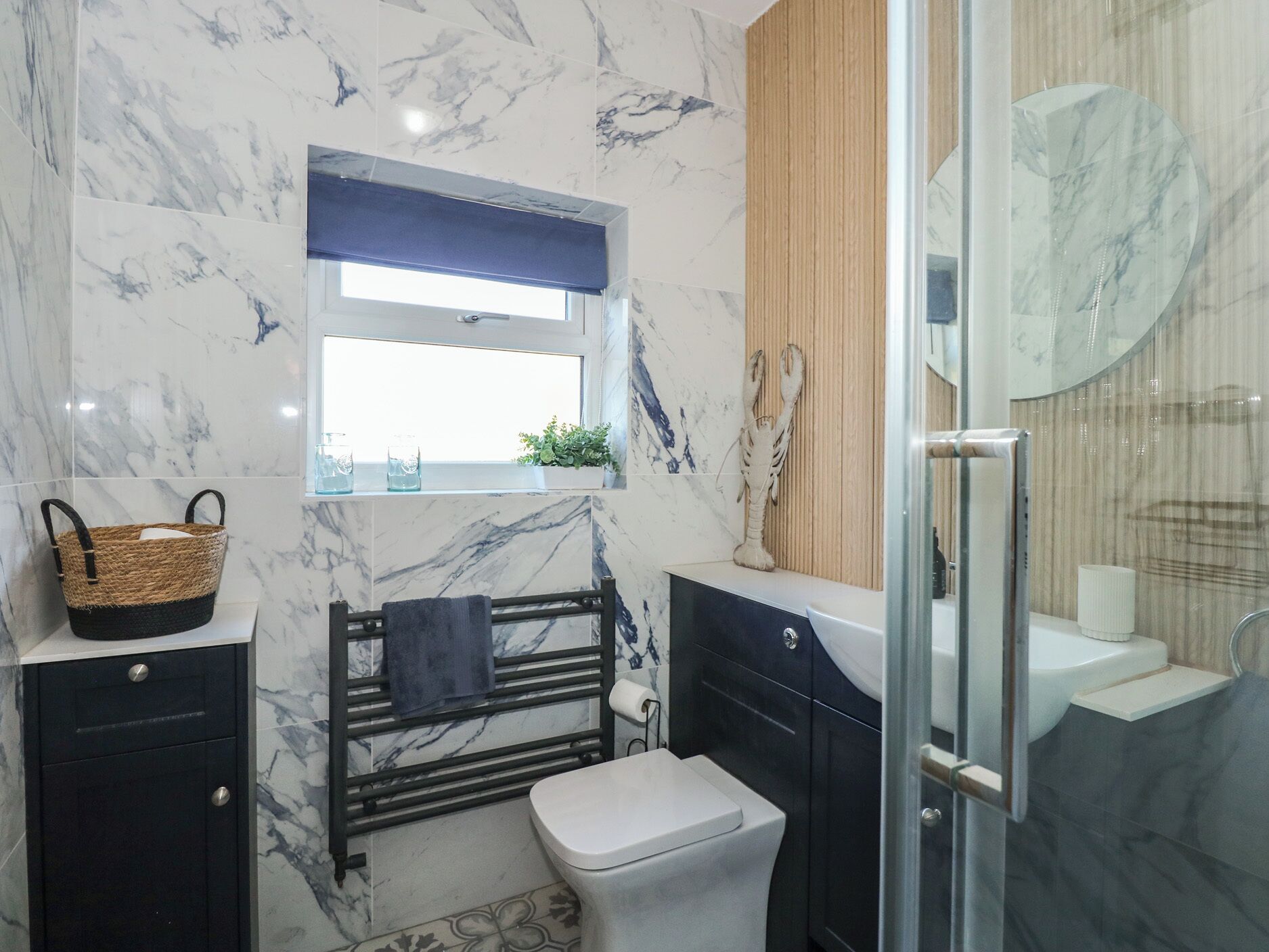 A bathroom with marble walls, a black vanity, a white toilet, a towel rack, and a glass shower enclosure.