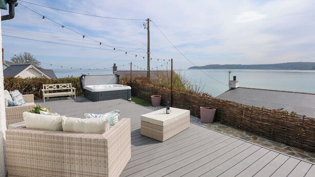 A deck with wicker furniture, a hot tub, and a view of the water. - Swn Y Wylan (Pentraeth)