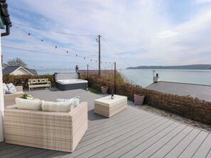 A deck with wicker furniture, a hot tub, and a view of the water. - Swn Y Wylan (Pentraeth)