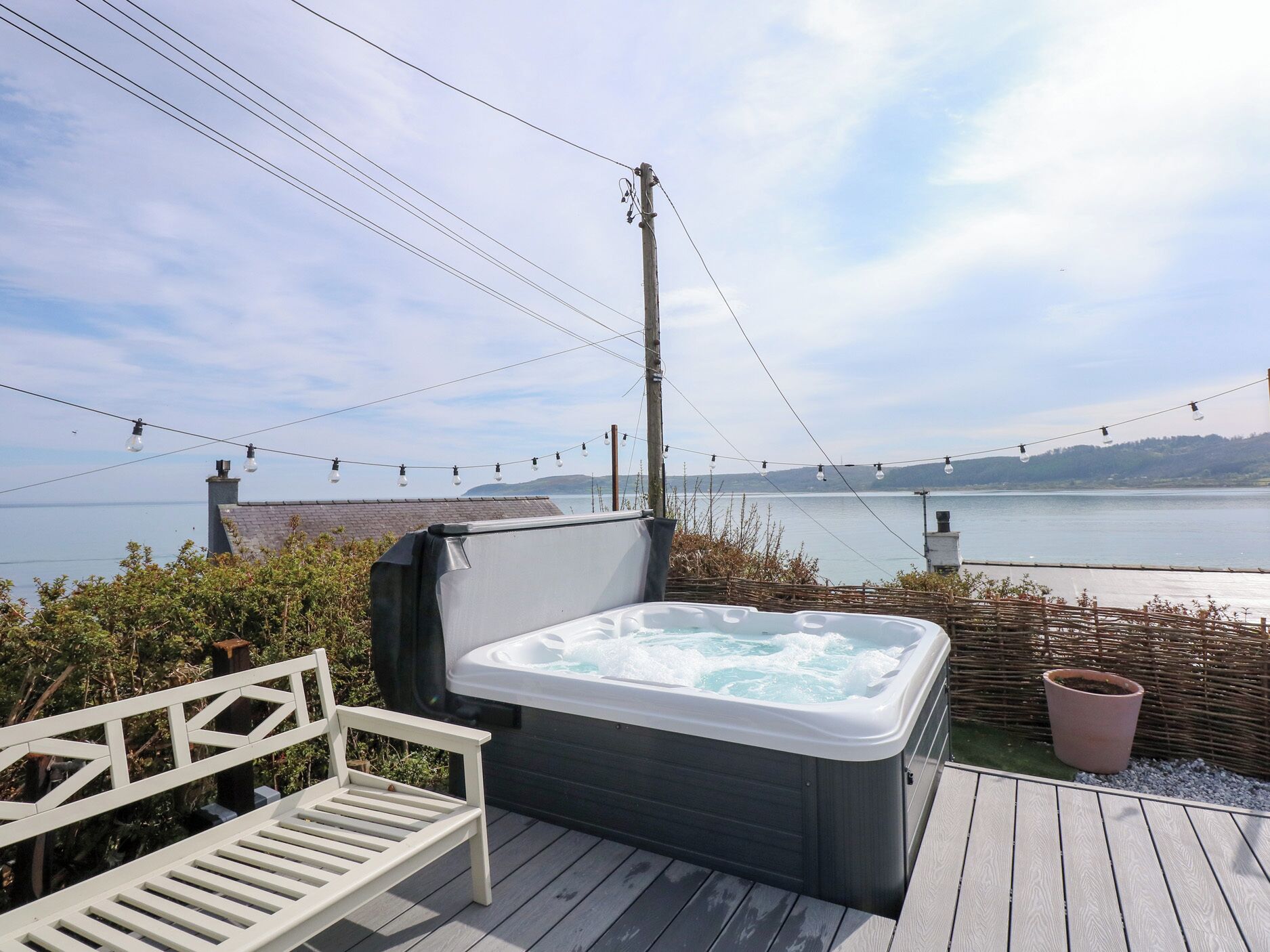 A hot tub on a wooden deck with a view of a lake and a bridge.