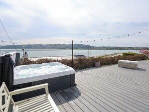 Un jacuzzi en una terraza de madera con vistas a un lago y colinas al fondo.