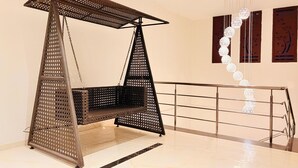A modern interior with a black wicker swing chair, a metal railing, and decorative spherical lights. - Wow Hotels (Tirupur)
