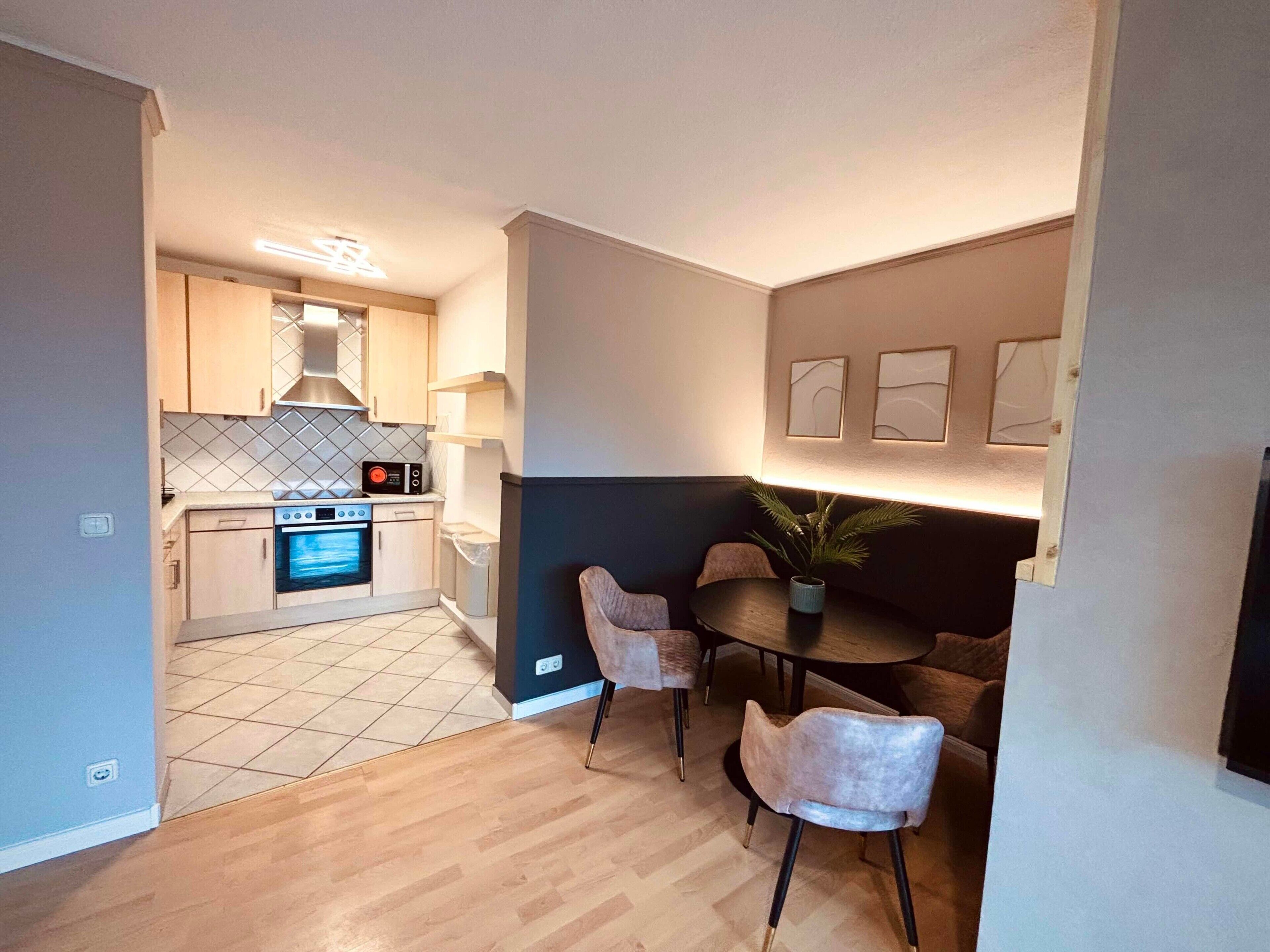 Een kleine keuken met moderne apparatuur, een eethoek met twee stoelen en een tafeltje.