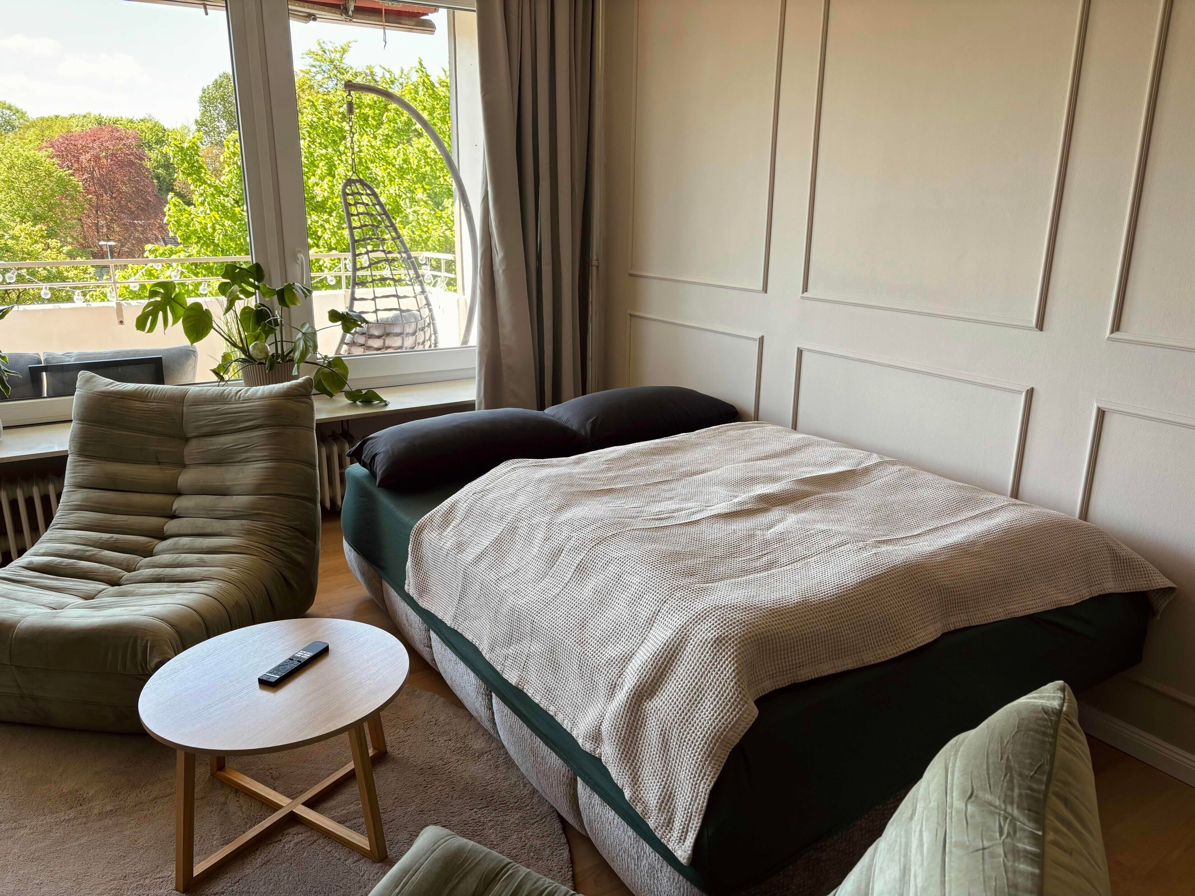 Un dormitorio con una cama, una silla, una mesita y vistas al exterior con vegetación.