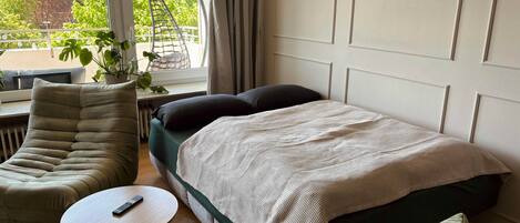 Un dormitorio con una cama, una silla, una mesita y vistas al exterior con vegetación.