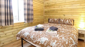 A wooden-paneled room with a bed, a window with curtains, and a bedside lamp. - Rabbit Warren Lodge (King's Lynn)