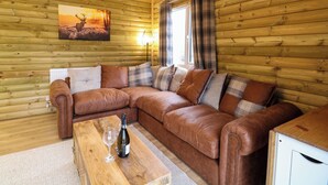 A cozy cabin interior with a brown leather sofa, a wooden coffee table, and a painting of a sunset. - Rabbit Warren Lodge (King's Lynn)