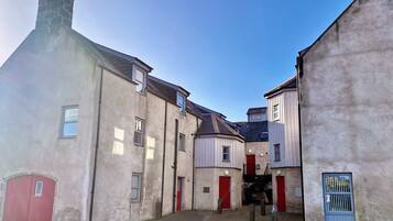 A narrow street with buildings on either side, featuring a red door and a staircase leading to an upper level.