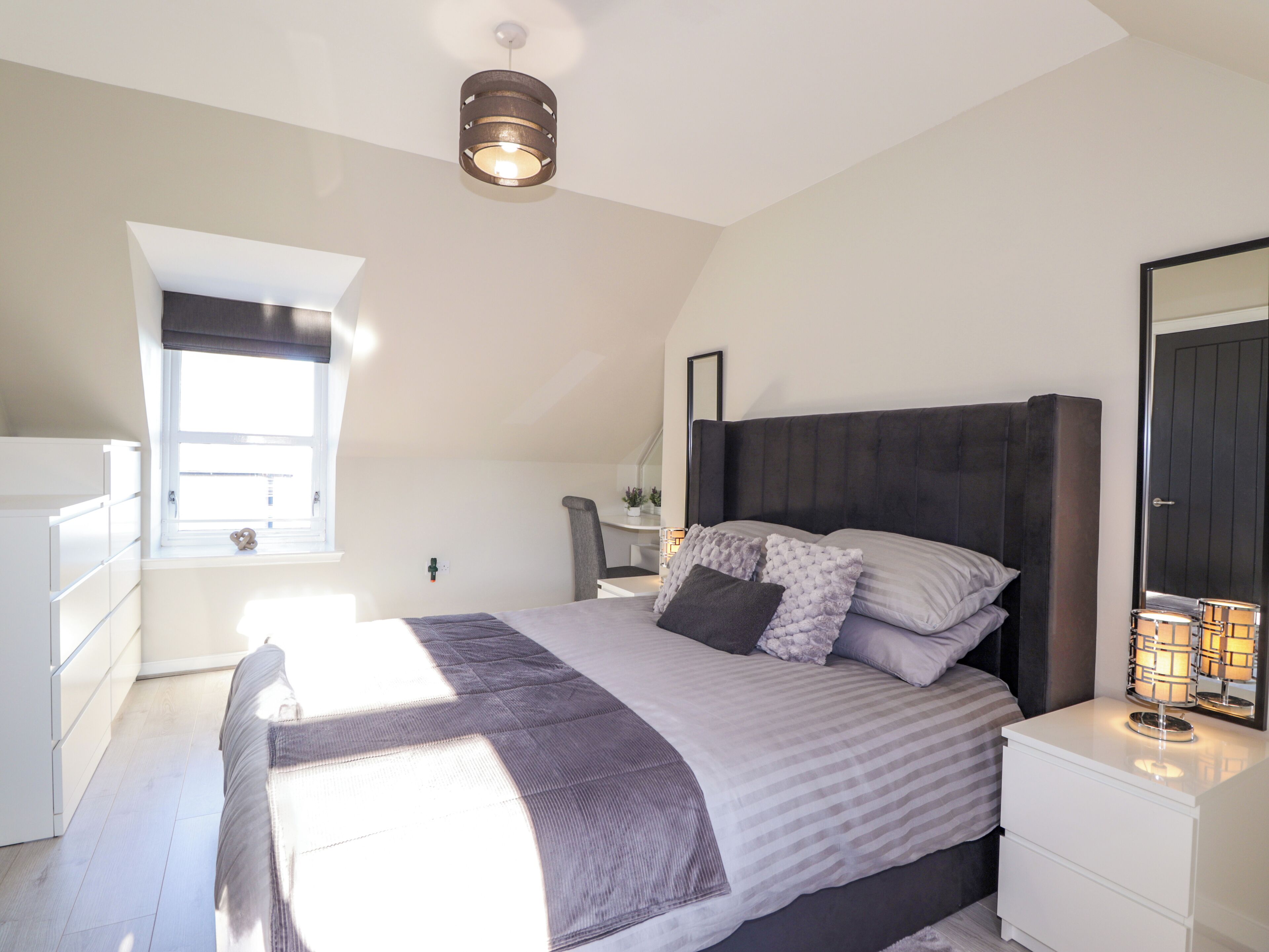 Een slaapkamer met een bed, nachtkastjes, een raam en een plafondlamp.