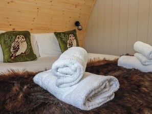 A cozy room with a wooden ceiling, a bed with white bedding and green pillows featuring owl designs, and a fur rug.