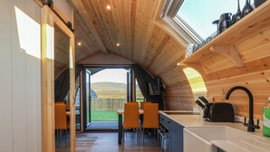 A cozy kitchen with wooden beams, a dining area with chairs, and a view of the outdoors. - Barn Owl (Carnforth)