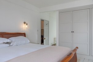 Un dormitorio con cama de madera, paredes blancas, un armario y una lámpara fijada a la pared.