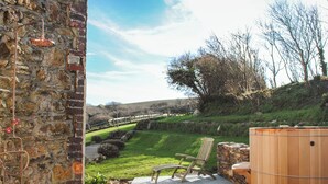 An outdoor patio with a stone wall, a wooden hot tub, and a wooden chair. - The Farmhouse at Broad Downs (Kingsbridge)