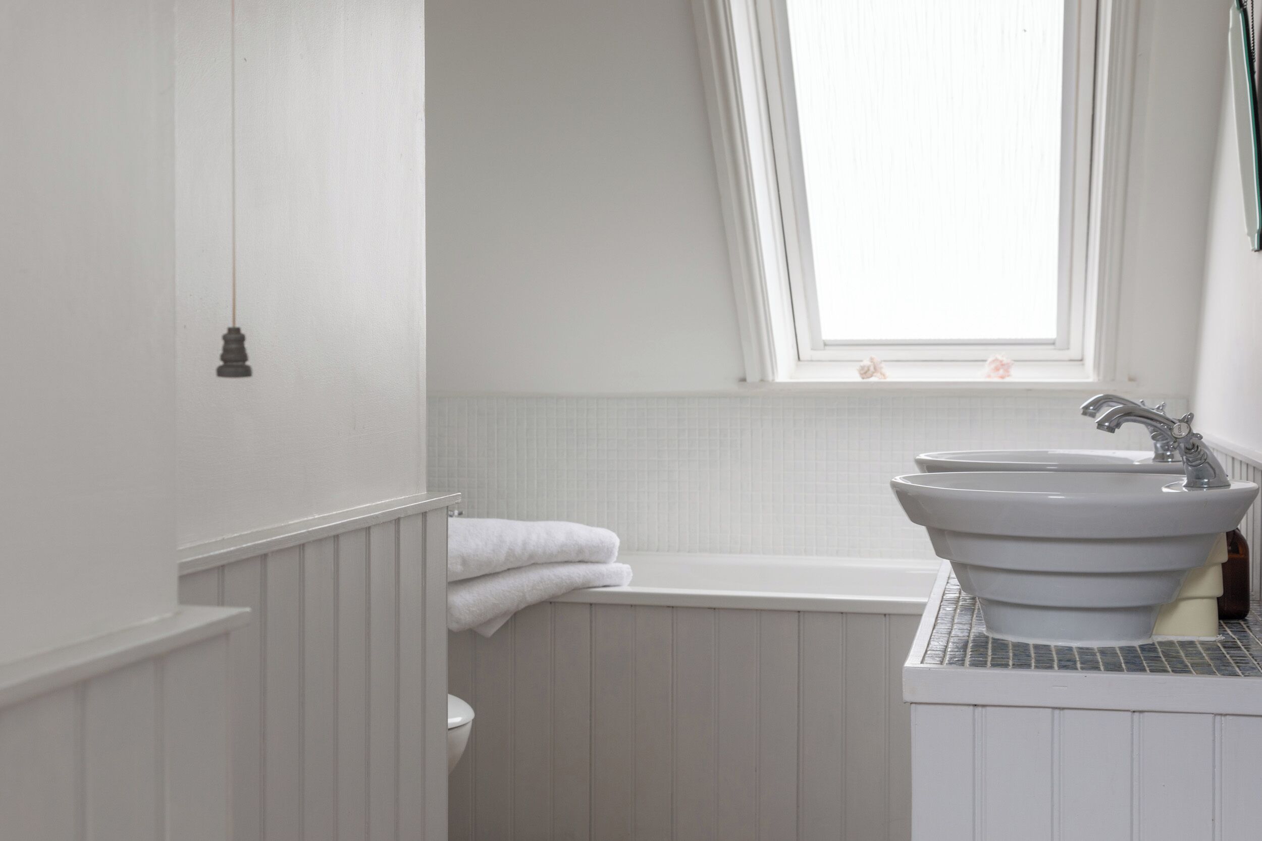 Un baño con una bañera blanca, un lavamanos blanco y una ventana sobre el lavamanos.