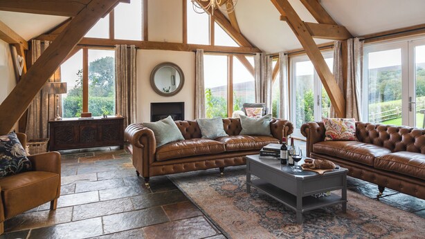 A spacious living room with a high ceiling and exposed wooden beams, furnished with leather sofas and a coffee table. - The Farmhouse at Broad Downs (Kingsbridge)