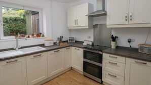 A modern kitchen with white cabinets, a stainless steel range hood, a built-in oven, and a window with potted plants. - Bryn Siriol (Narberth)