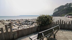 A wooden bench by a rocky beach with a wooden fence and a small bush. - Bryn Siriol (Narberth)