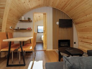 A cozy, semi-open living space with a curved wooden ceiling, a fireplace, a television mounted on the wall, and a dining area with a table and chairs.