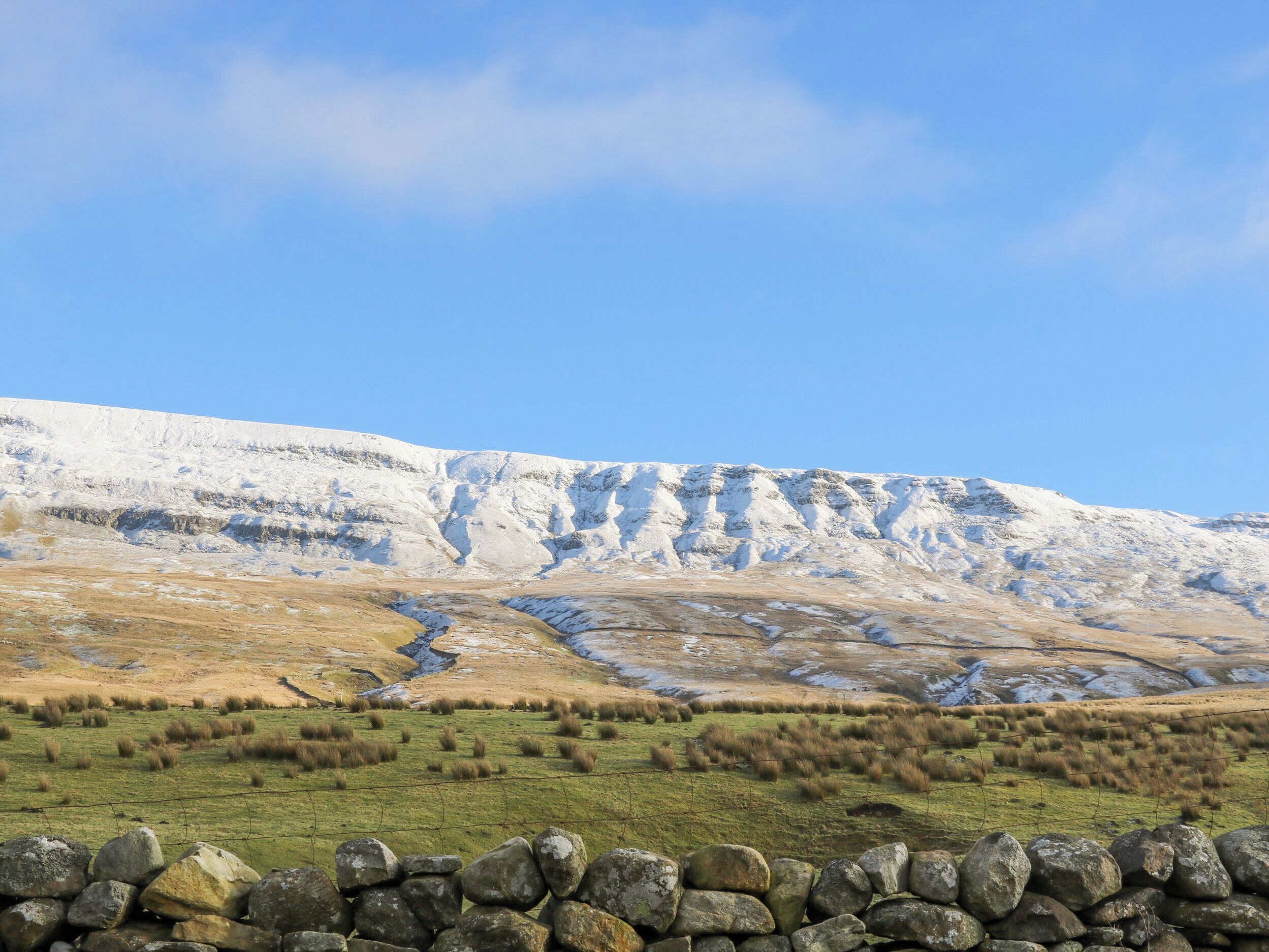 Un muro de piedra en primer plano con una vista despejada de una colina cubierta de nieve al fondo.