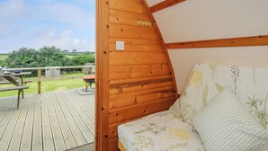 Eine Holzhütte mit Bett, Fenster und Blick auf eine Wiese mit Picknicktisch.
