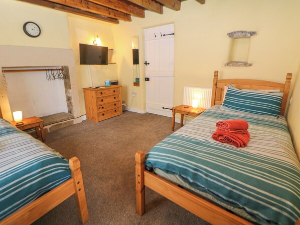 Ein Schlafzimmer mit zwei Holzbetten, einer Holzkommode, einem Nachttisch mit Lampe, einem an der Wand befestigten Fernseher und einer Wanduhr.