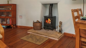 A cozy living room with a wood-burning stove, a wooden cabinet, and a dining area.
