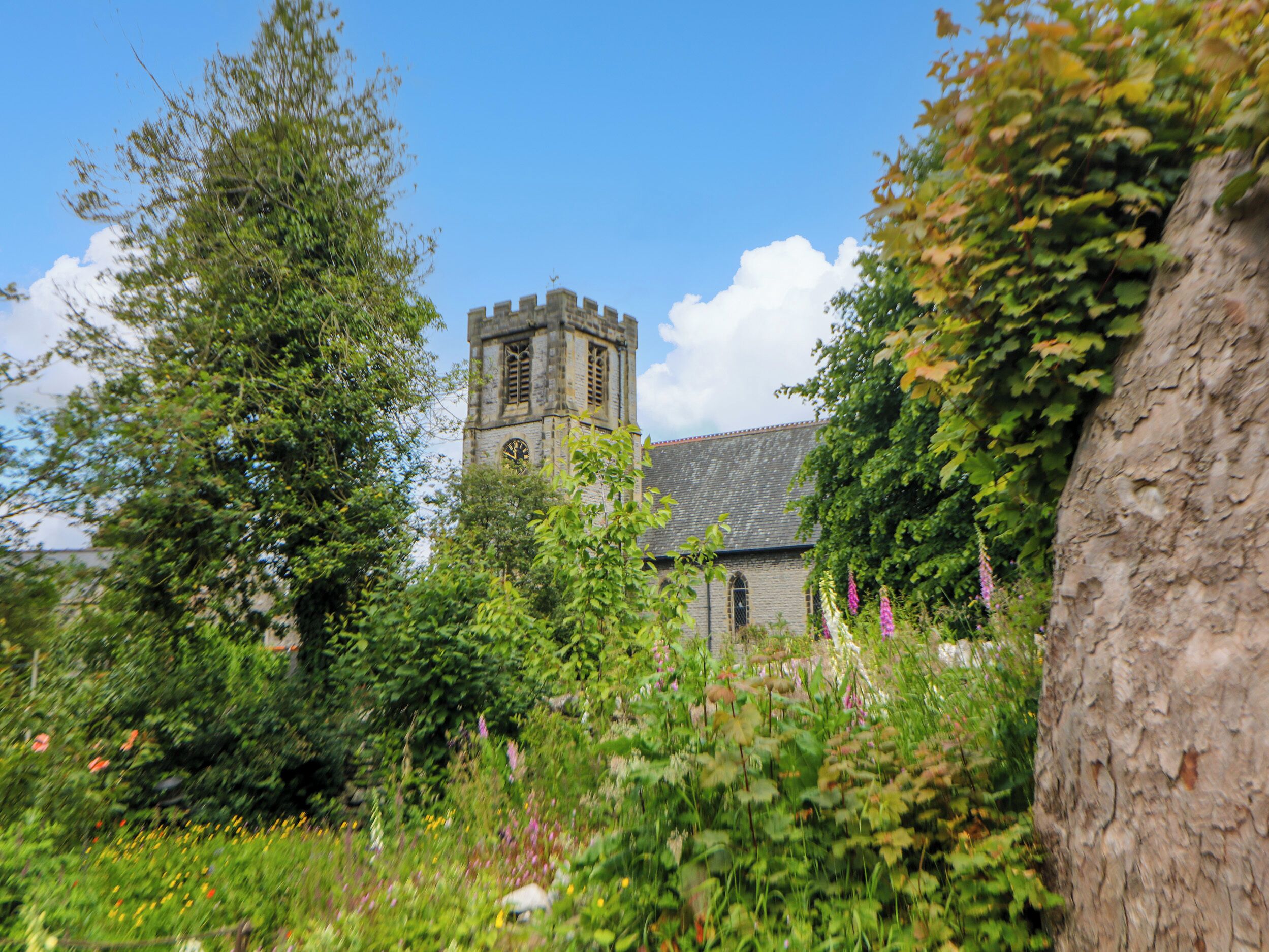 Una iglesia histórica con un campanario, rodeada de exuberante vegetación y plantas florecientes.
