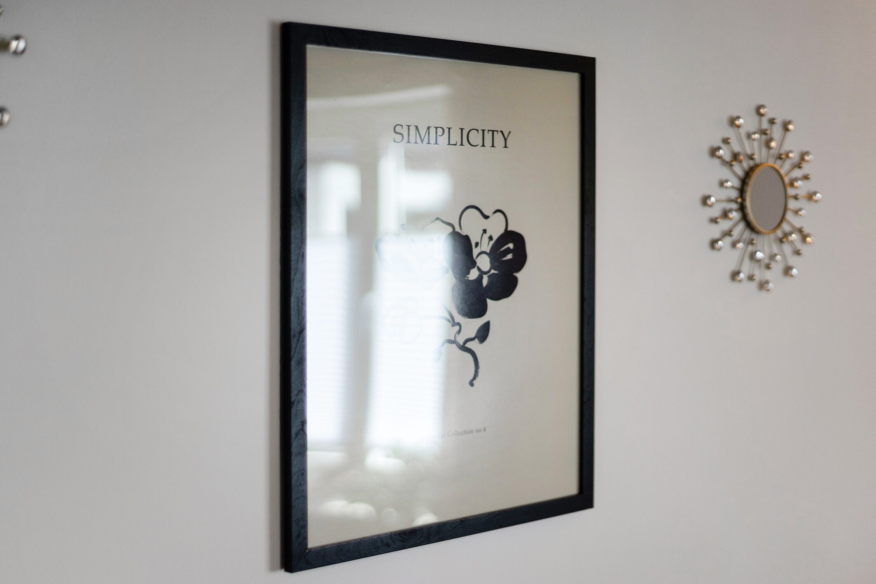 Una obra de arte enmarco con la palabra 'SIMPlicity' y un diseño floral en una pared.