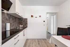 A modern kitchen with white cabinets, a black countertop, and a wooden floor. There are three framed pictures on the wall.