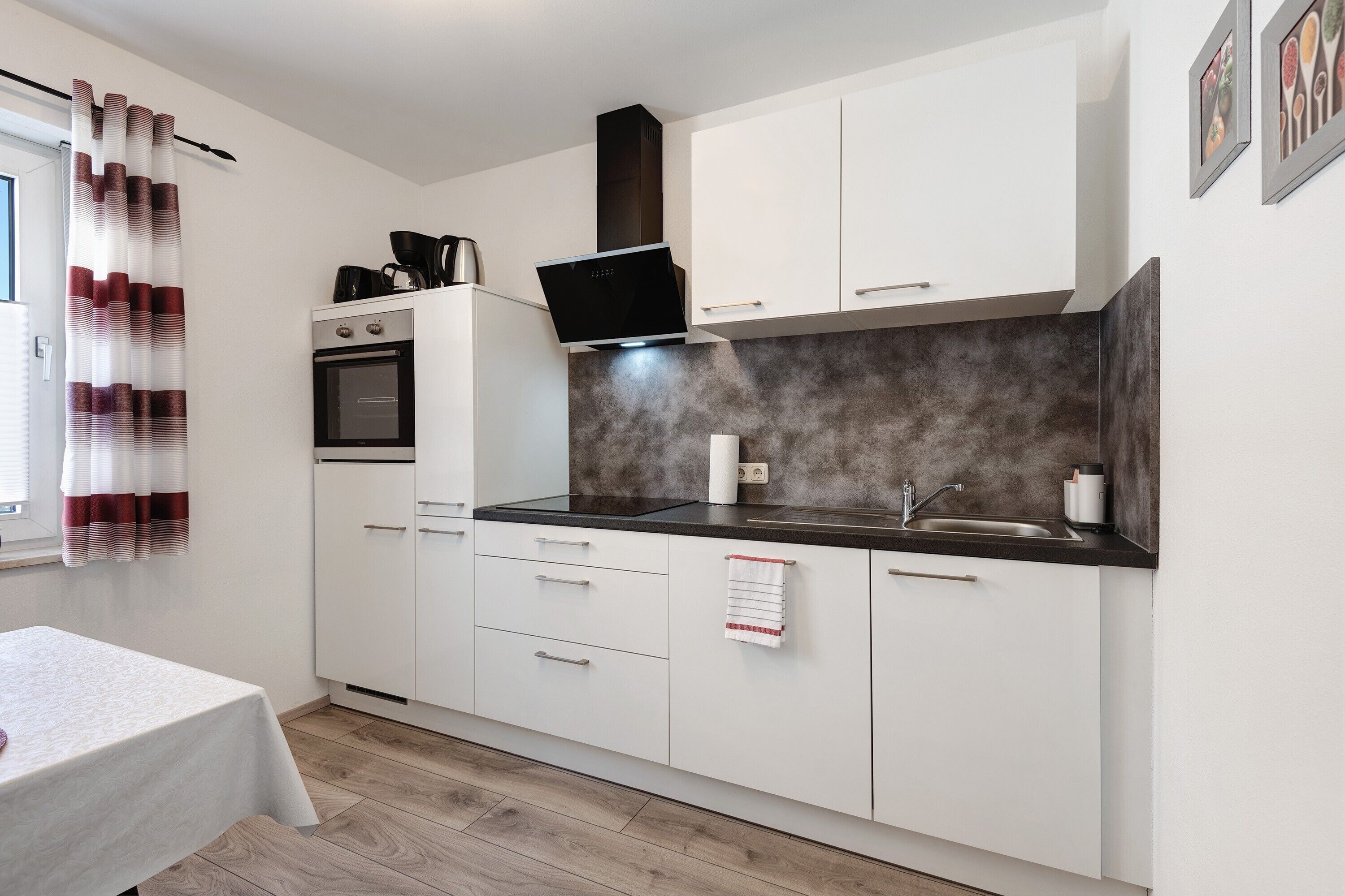 A compact kitchen with white cabinets, a black countertop, a built-in oven, and a stainless steel sink.