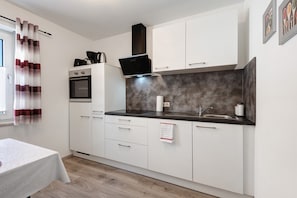A compact kitchen with white cabinets, a black countertop, a built-in oven, and a stainless steel sink.