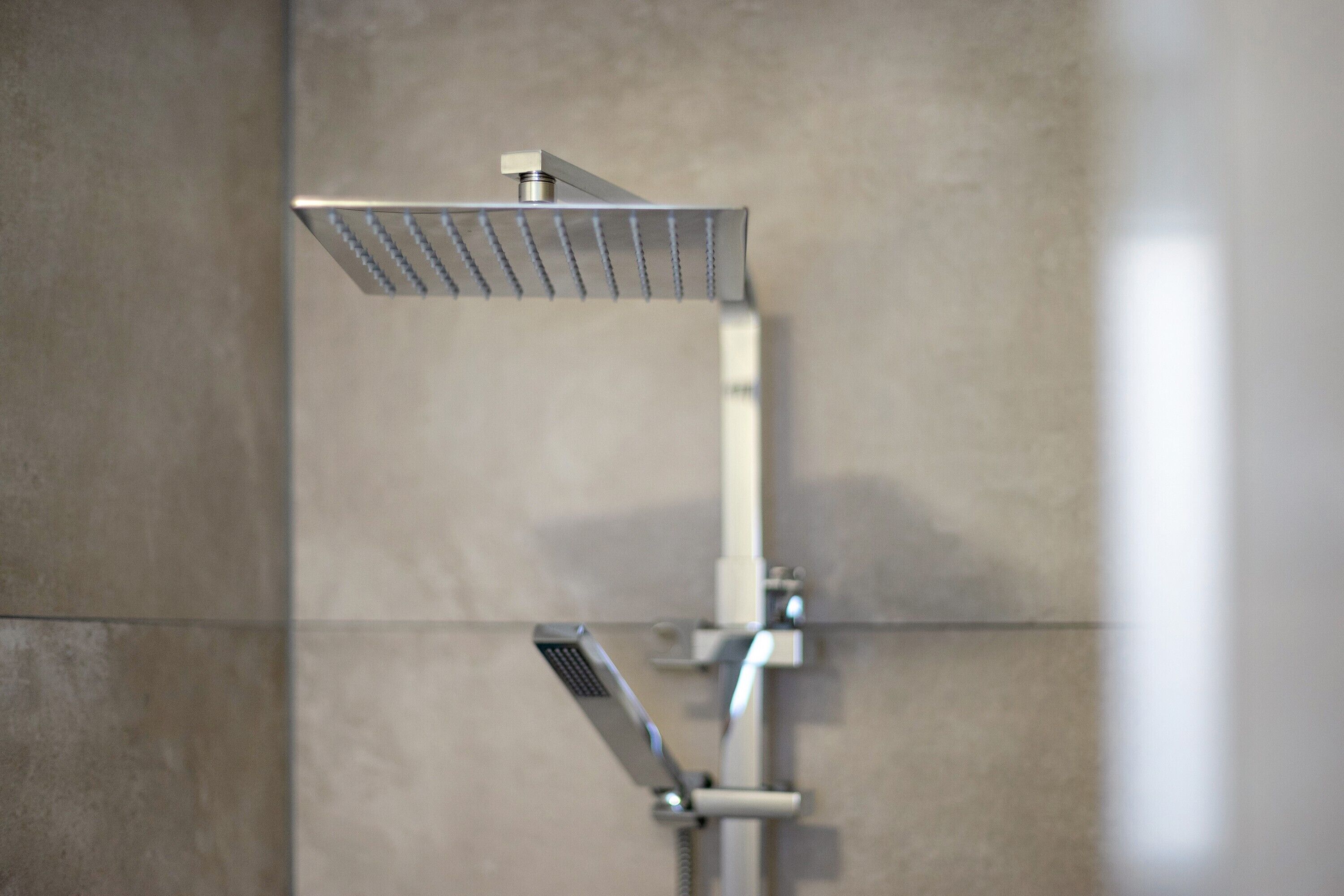 Un cabezal de ducha moderno con diseño rectangular, instalado en una pared con superficie de azulejos lisos.