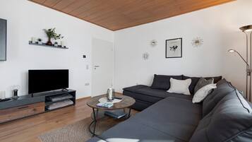 Ein modernes Wohnzimmer mit Flachbildfernseher, dunklem Sofa, Couchtisch und Holzboden.