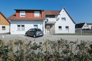A two-story residential building with a car parked in the driveway, a satellite dish, and a gated entrance.
