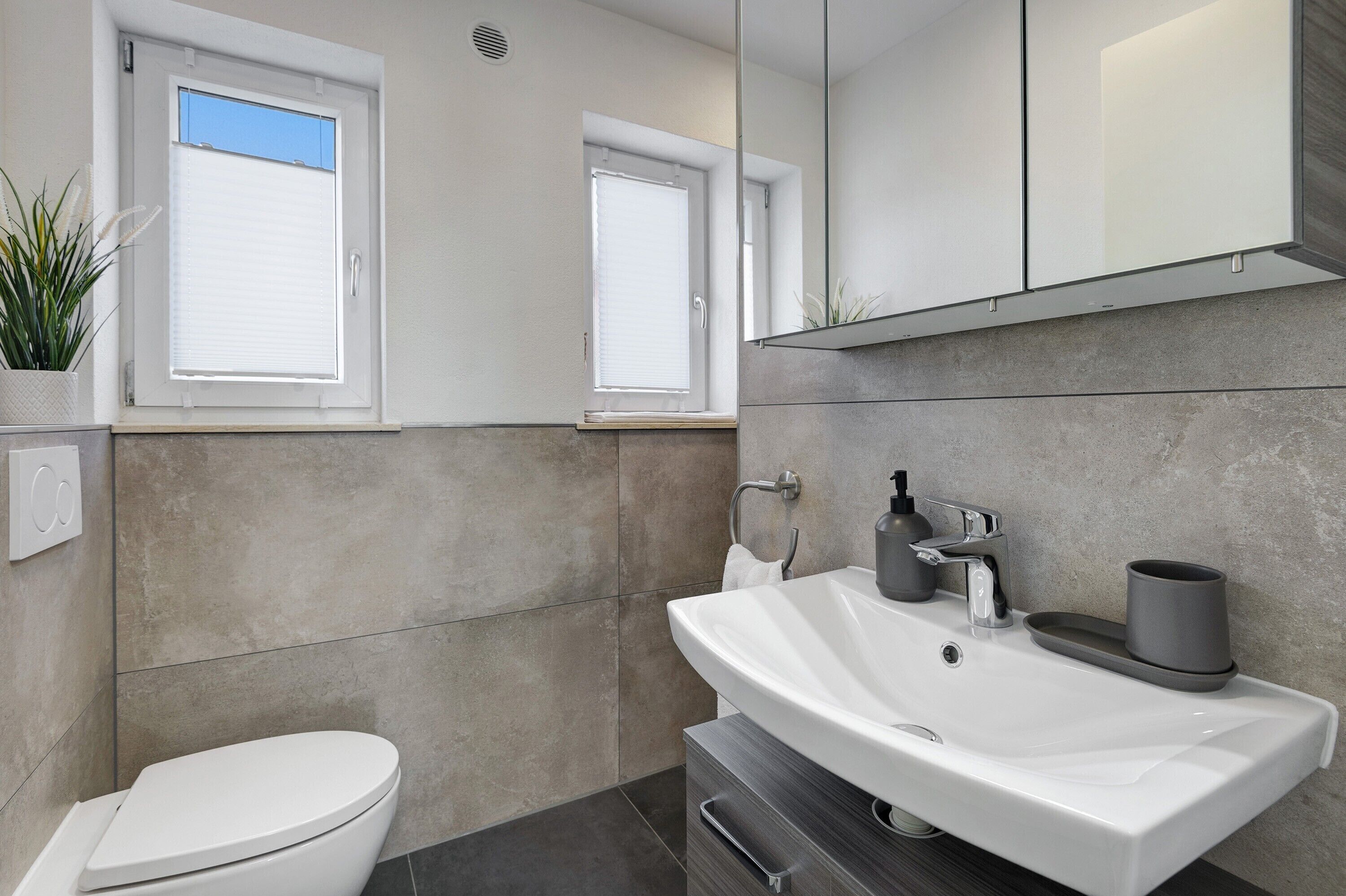 Un baño moderno con un lavamanos blanco, un inodoro y una ventana con persianas.