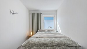 Un dormitorio con cama, una ventana con persianas, una lámpara de noche y una pared con un nombre.