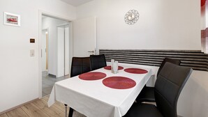 Un comedor con una mesa blanca, individuales rojos, sillas negras y un elemento decorativo en la pared.