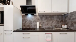 Una cocina moderna con armarios blancos, encimera negra, pileta de acero inoxidable y horno empotrado.