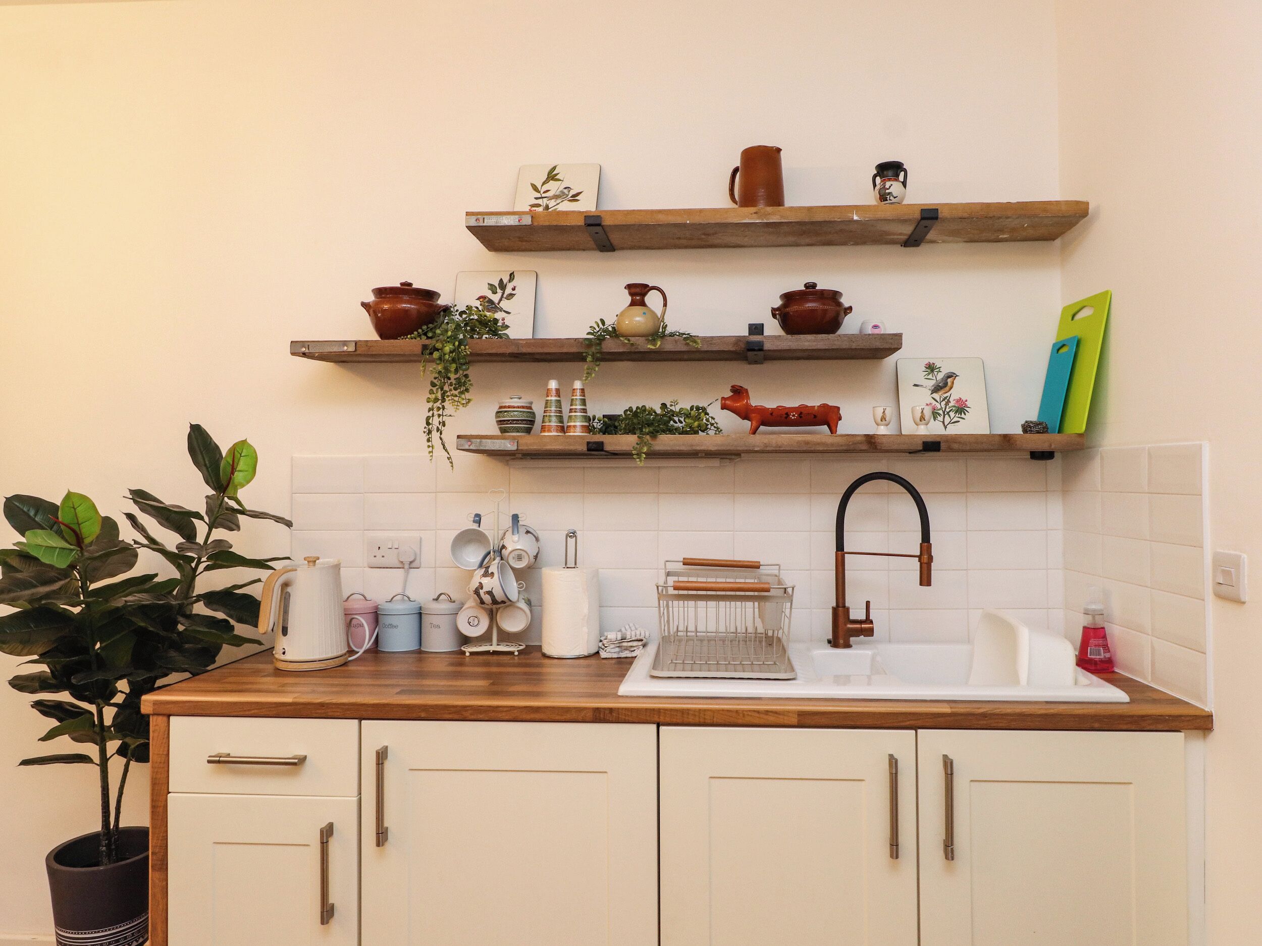 Una cocina con estantes de madera, un fregadero y distintos utensilios.