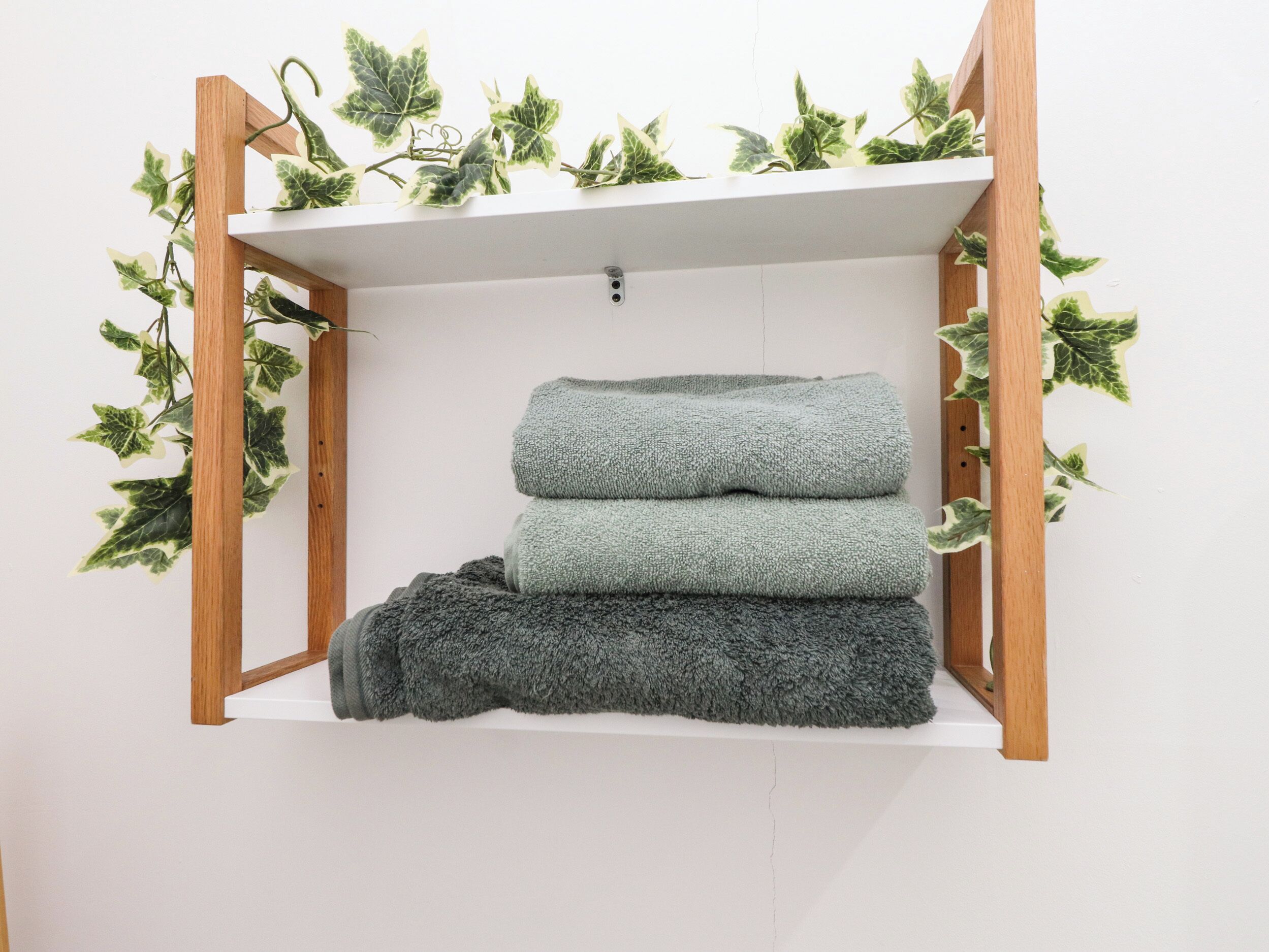 A shelf with three folded towels and green foliage.