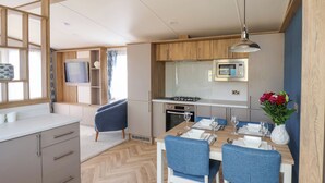 A modern kitchen with a microwave, stove, and dining area with blue chairs and a table set for two.