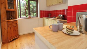 Eine Küche mit Holzausstattung, einem Fenster mit Blick auf Grünflächen, einer roten Fliesenrückwand und einem Toaster auf der Arbeitsplatte.
