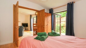 Ein Schlafzimmer mit einer rosa Bettdecke, grünen Handtüchern, Holzmöbeln und Blick ins Grüne.
