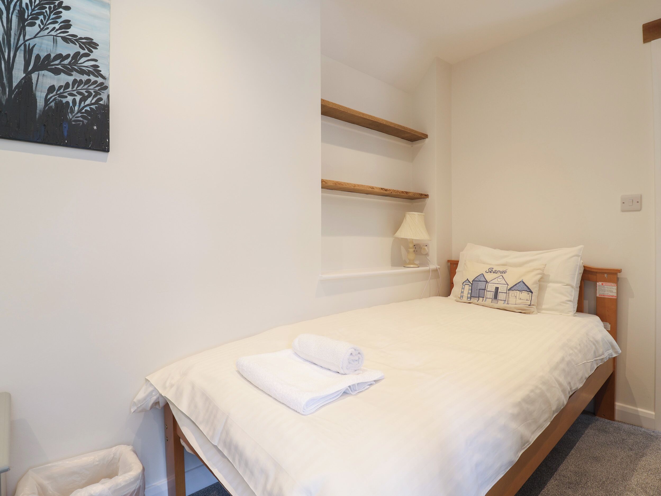 A neatly made bed with white bedding and a rolled towel, a bedside lamp, and a pillow with a house design.