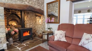 A cozy living room with a stone fireplace, a red sofa, and a wooden coffee table. - Myrtle Cottage (Lyme Regis)