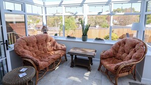 A conservatory with two wicker chairs, a small table, and potted plants. - Myrtle Cottage (Lyme Regis)