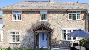 A stone house with a white door, multiple windows, and a small porch area. - Myrtle Cottage (Lyme Regis)