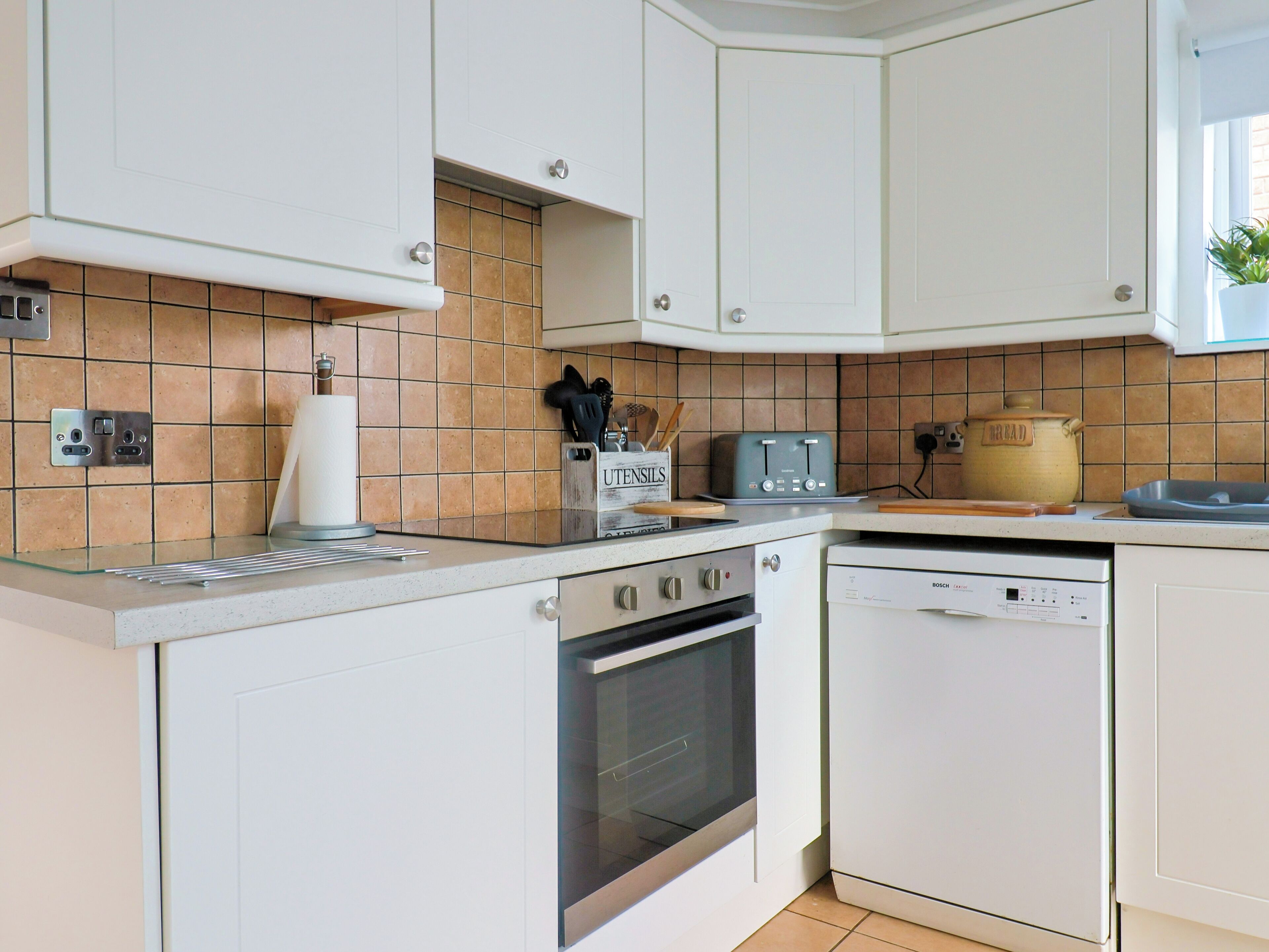 A modern kitchen with white cabinets, a built-in oven, a dishwasher, and a tiled backsplash.